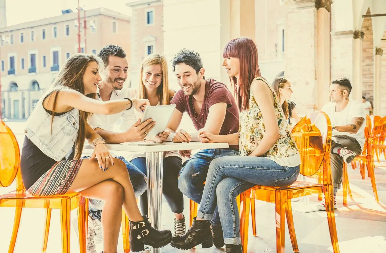 Group of students sitting in a cafe bar looking at tablet - Young cheerful friends having fun with portable computer - Active people watching a funny streaming movie online (Group of students sitting in a cafe bar looking at tablet - Young cheerful fr